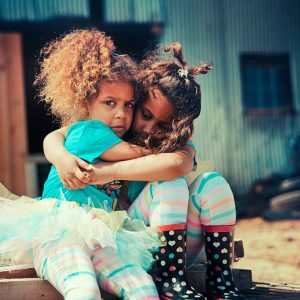 Two young girls hug and comfort each other outside